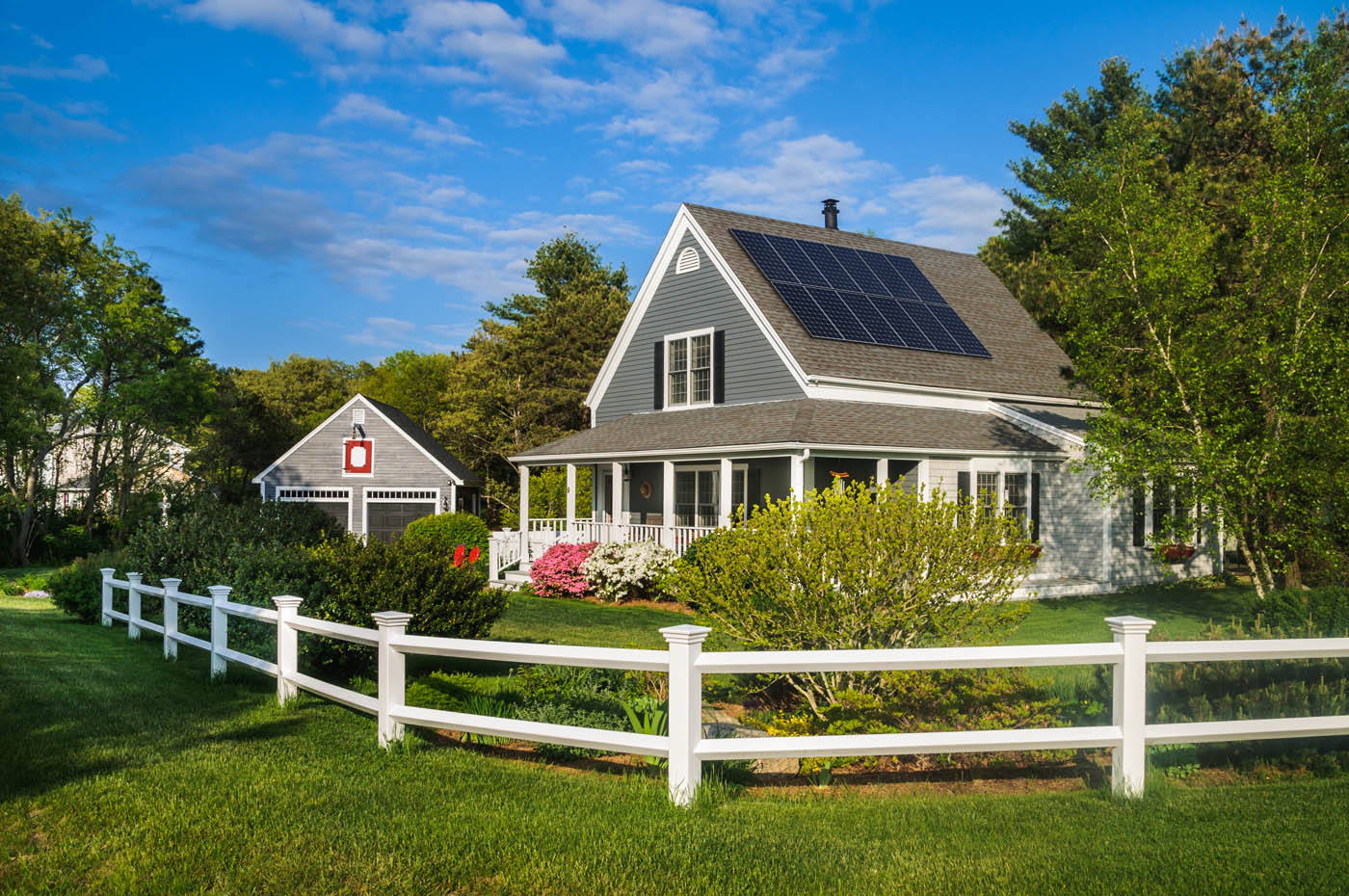 A large house with a white fence with solar panels installed.